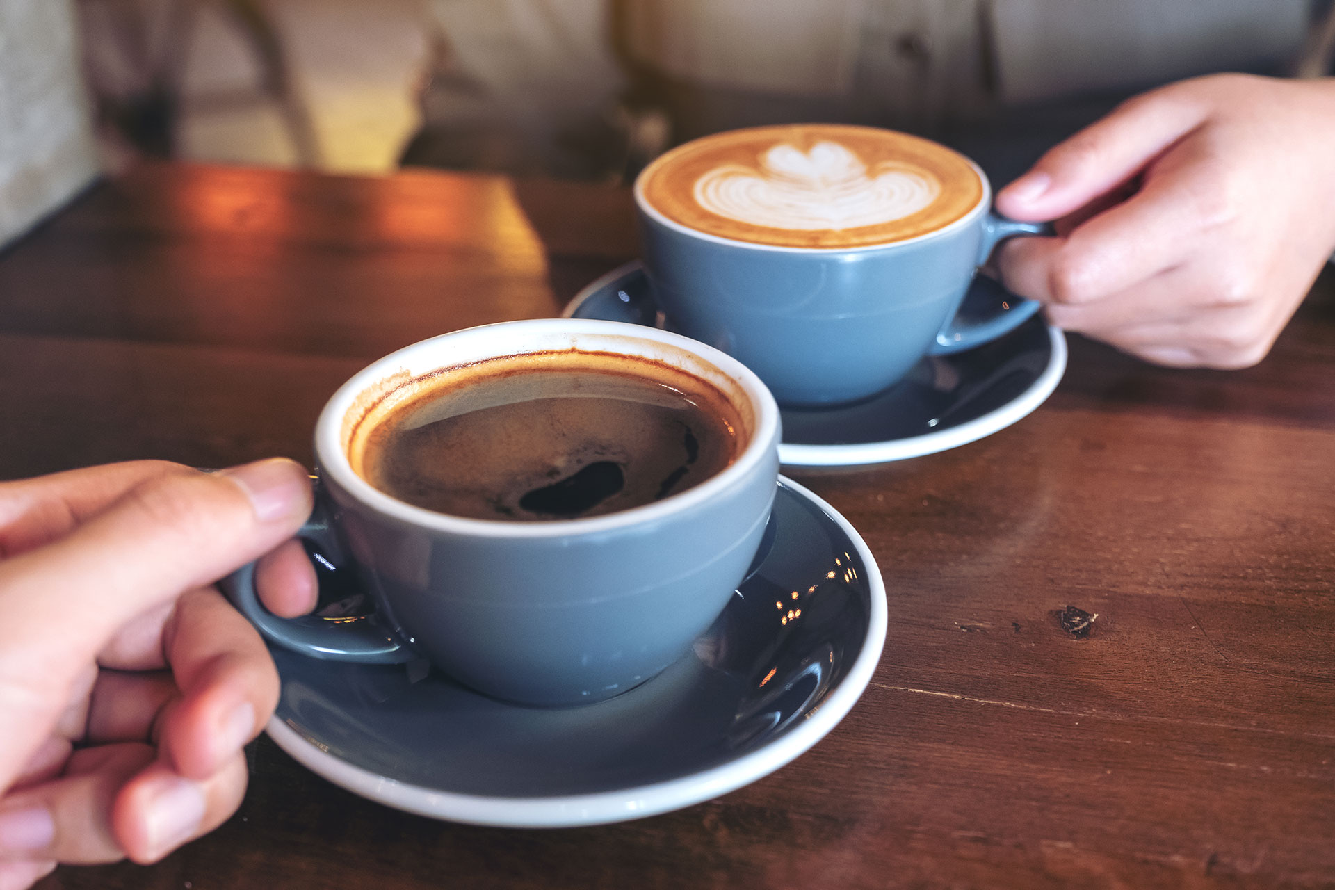 Two hands holding coffee cups placed on a table