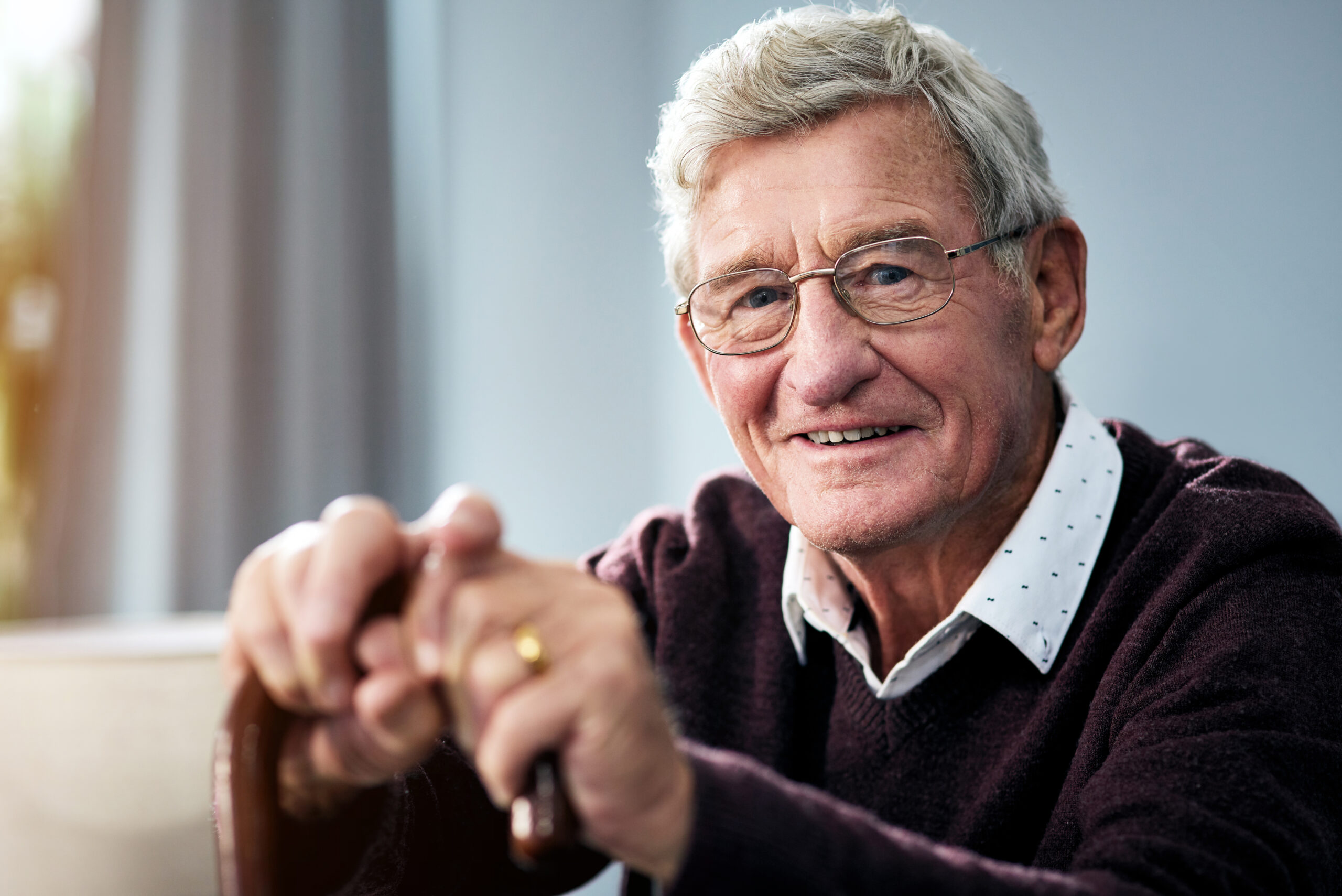 Portrait of a senior man sitting at home with a walking stick